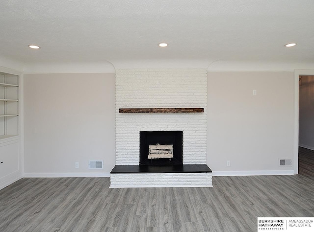 unfurnished living room with wood-type flooring, built in features, and a brick fireplace