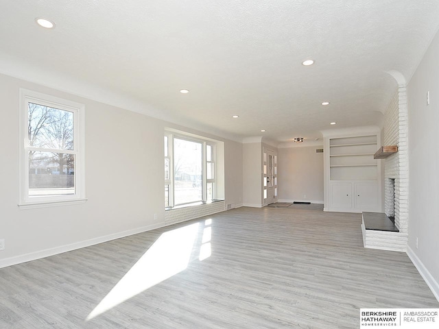 unfurnished living room with light hardwood / wood-style floors, built in features, a textured ceiling, and a brick fireplace