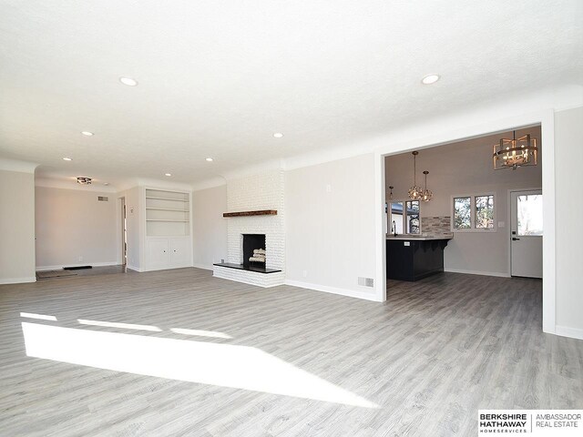 unfurnished living room featuring a notable chandelier, light wood-type flooring, built in features, and a brick fireplace