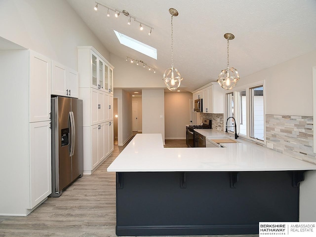 kitchen featuring kitchen peninsula, a kitchen bar, stainless steel appliances, sink, and white cabinets