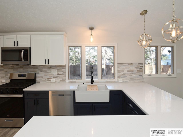 kitchen with sink, tasteful backsplash, decorative light fixtures, white cabinets, and appliances with stainless steel finishes