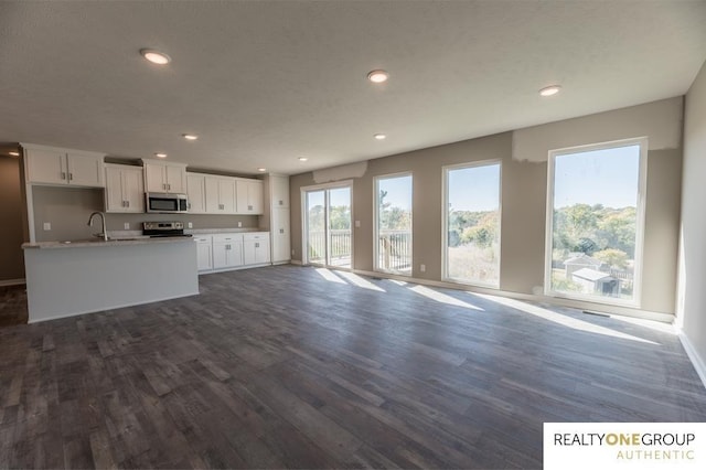 kitchen with sink, dark wood-type flooring, a center island with sink, white cabinets, and appliances with stainless steel finishes