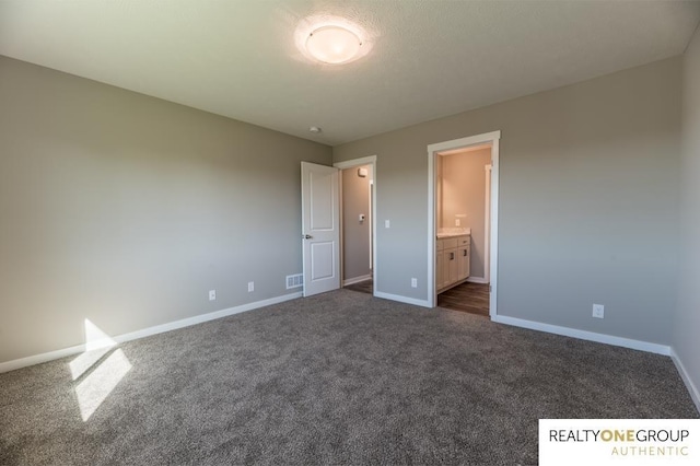 unfurnished bedroom featuring ensuite bathroom and dark carpet