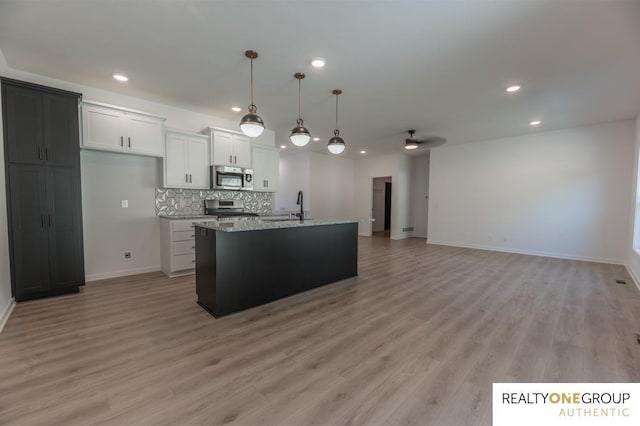 kitchen featuring ceiling fan, an island with sink, light stone counters, white cabinetry, and stainless steel appliances