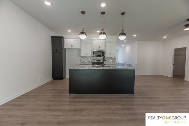 kitchen with a center island with sink, light stone countertops, tasteful backsplash, white cabinetry, and stainless steel appliances