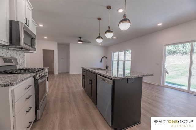 kitchen with white cabinetry, sink, decorative light fixtures, a center island with sink, and appliances with stainless steel finishes