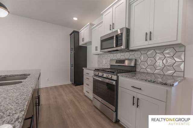 kitchen featuring decorative backsplash, light stone countertops, appliances with stainless steel finishes, light hardwood / wood-style floors, and white cabinetry