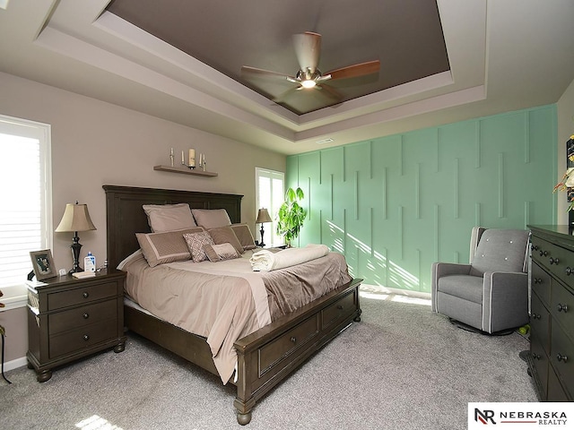 bedroom with light carpet, a tray ceiling, and ceiling fan