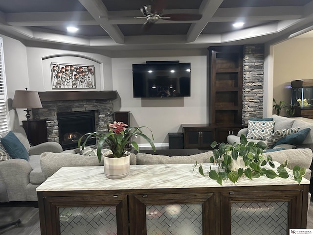 living room featuring beamed ceiling, ceiling fan, coffered ceiling, and a stone fireplace