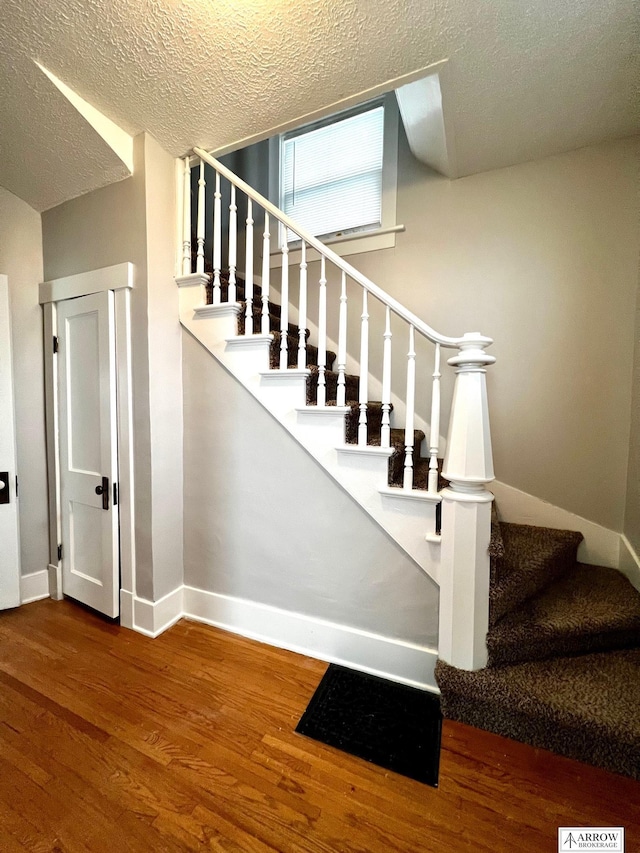 staircase with wood-type flooring and a textured ceiling