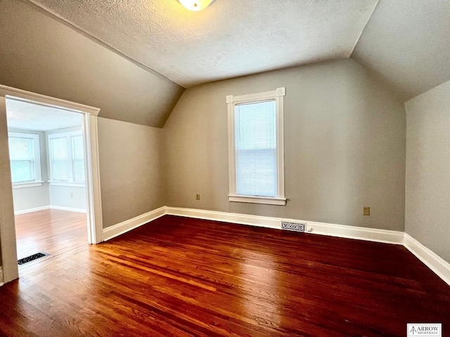 additional living space featuring hardwood / wood-style flooring, a textured ceiling, and vaulted ceiling