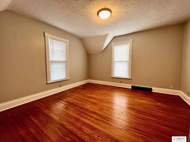 additional living space featuring a textured ceiling, lofted ceiling, and dark wood-type flooring