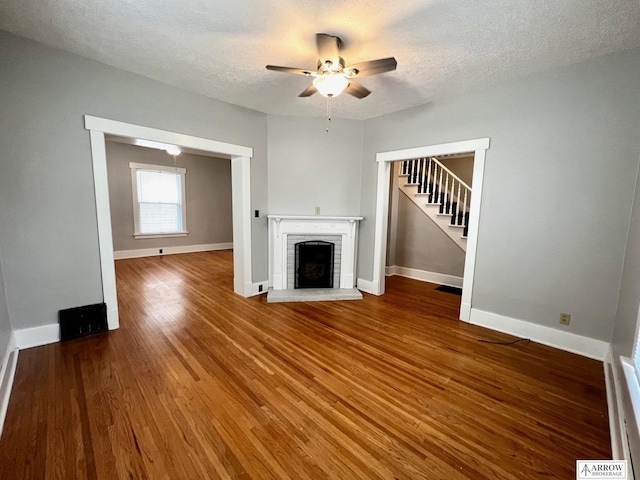 unfurnished living room with a brick fireplace, ceiling fan, a textured ceiling, and hardwood / wood-style flooring