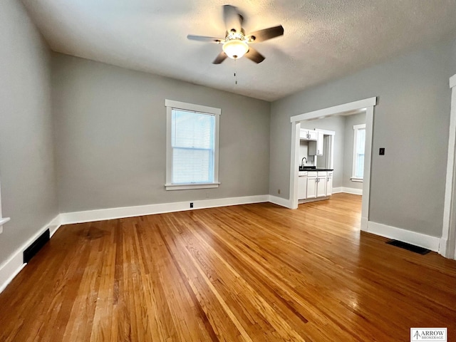 unfurnished living room featuring ceiling fan, light hardwood / wood-style flooring, a textured ceiling, and sink