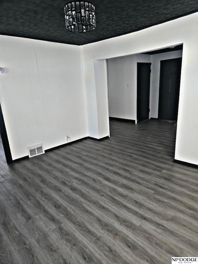 unfurnished room with a notable chandelier and dark wood-type flooring