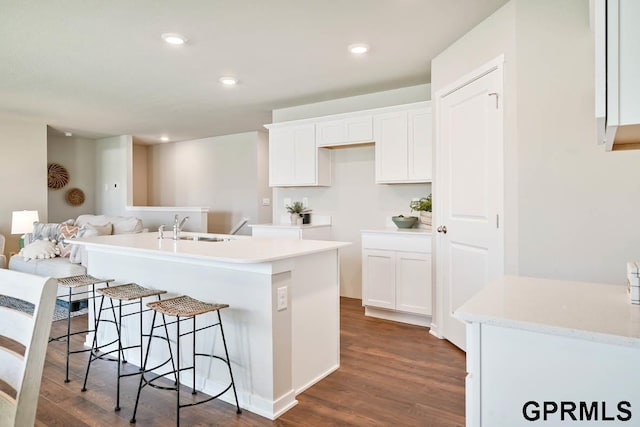 kitchen featuring sink, white cabinetry, dark wood-type flooring, and an island with sink