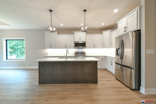 kitchen featuring white cabinetry, sink, stainless steel appliances, an island with sink, and decorative light fixtures