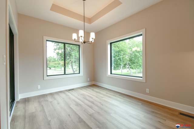 unfurnished room featuring a chandelier, light hardwood / wood-style flooring, and a tray ceiling