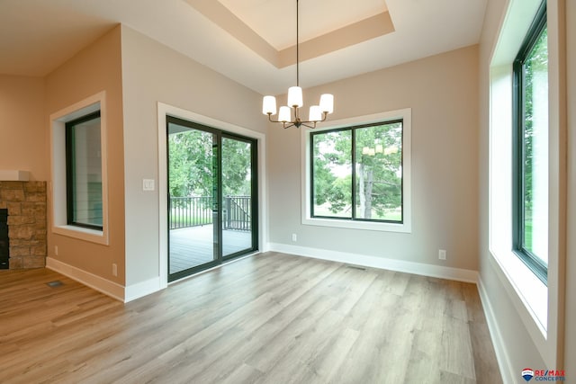 interior space with a fireplace, light wood-type flooring, a raised ceiling, and a notable chandelier