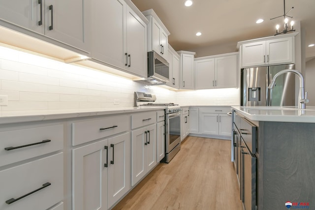 kitchen with white cabinets, decorative light fixtures, stainless steel appliances, and light hardwood / wood-style floors