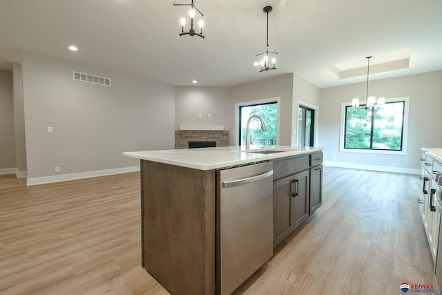 kitchen with stainless steel dishwasher, sink, decorative light fixtures, a center island with sink, and light hardwood / wood-style floors