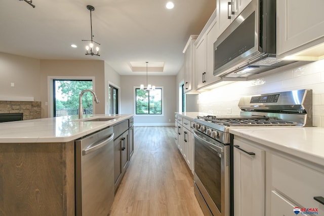 kitchen with stainless steel appliances, sink, white cabinets, a chandelier, and hanging light fixtures