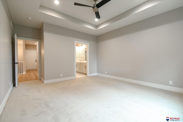 unfurnished bedroom with ensuite bathroom, a raised ceiling, ceiling fan, and light colored carpet