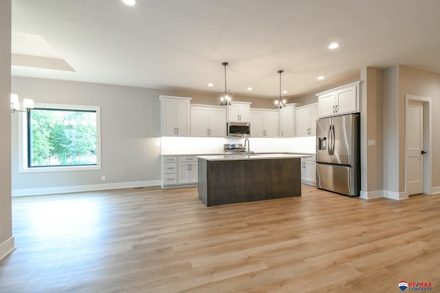 kitchen featuring appliances with stainless steel finishes, light hardwood / wood-style flooring, white cabinets, hanging light fixtures, and an island with sink