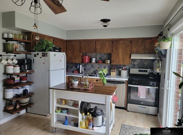 kitchen featuring appliances with stainless steel finishes, backsplash, decorative light fixtures, and light hardwood / wood-style flooring