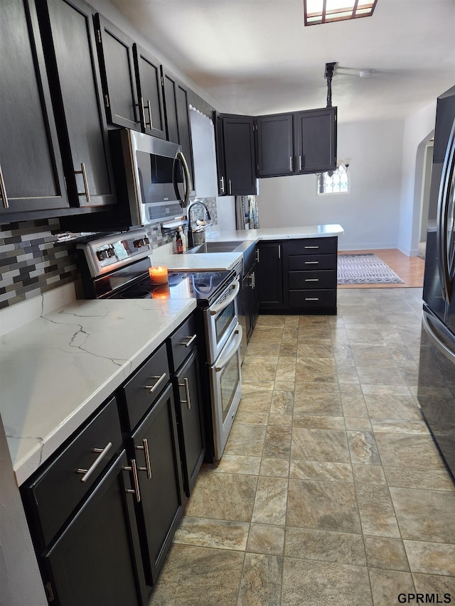 kitchen with sink, hanging light fixtures, decorative backsplash, light stone countertops, and stainless steel appliances