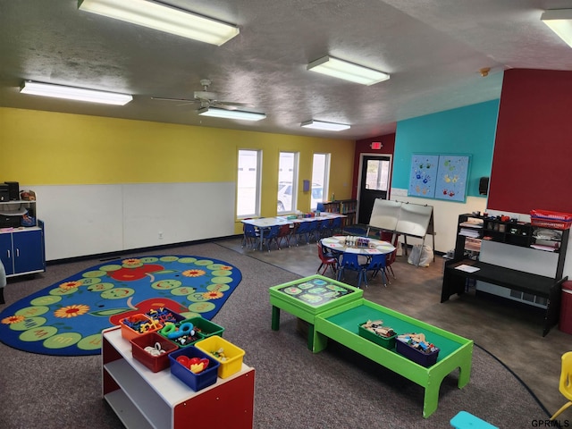 recreation room with a textured ceiling, ceiling fan, dark carpet, and vaulted ceiling