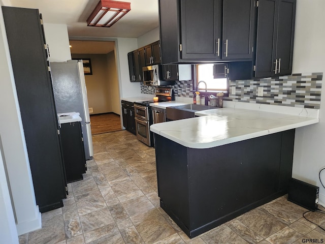 kitchen with light stone counters, kitchen peninsula, sink, and appliances with stainless steel finishes