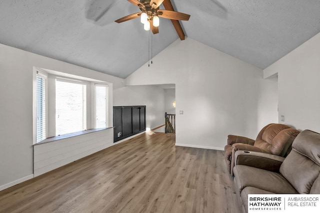 living room with vaulted ceiling with beams, ceiling fan, a textured ceiling, and light hardwood / wood-style flooring