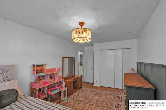 bedroom with a closet, light hardwood / wood-style floors, a textured ceiling, and an inviting chandelier