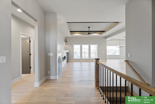 hallway with light hardwood / wood-style floors, a raised ceiling, and an inviting chandelier