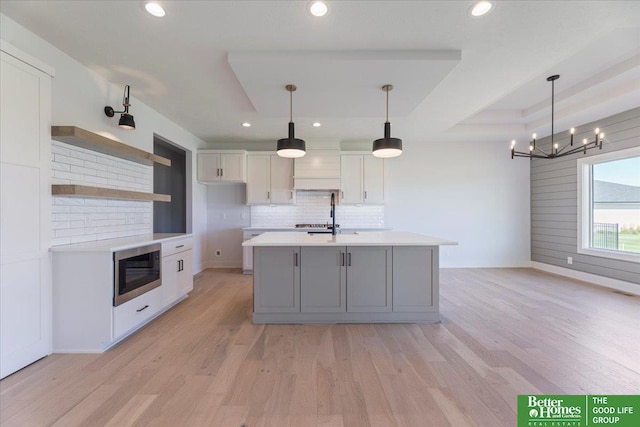 kitchen featuring black microwave, hanging light fixtures, white cabinets, and an island with sink