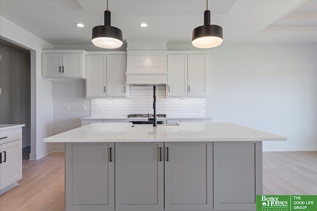 kitchen featuring backsplash, hanging light fixtures, light hardwood / wood-style floors, stainless steel gas stovetop, and an island with sink