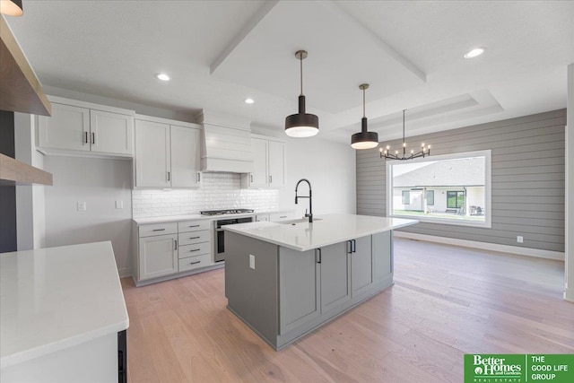 kitchen featuring an island with sink, decorative light fixtures, a tray ceiling, custom range hood, and appliances with stainless steel finishes