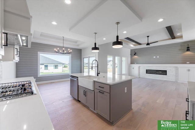 kitchen with a raised ceiling, gray cabinets, stainless steel dishwasher, and ceiling fan with notable chandelier