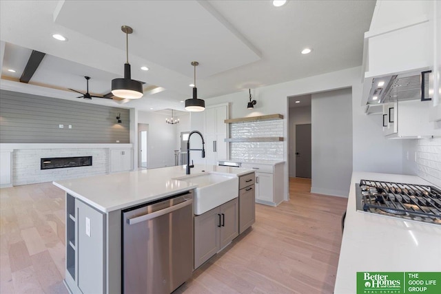 kitchen featuring gray cabinetry, a center island with sink, hanging light fixtures, a fireplace, and appliances with stainless steel finishes