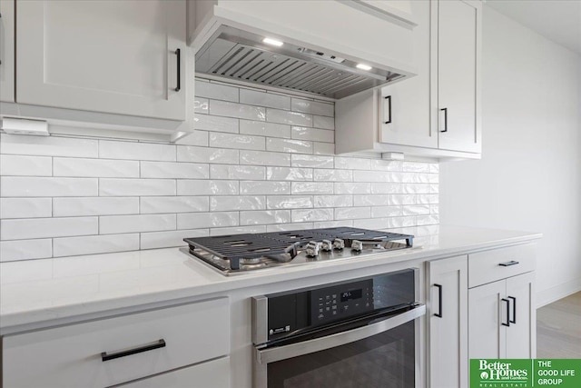 kitchen featuring ventilation hood, decorative backsplash, light stone countertops, appliances with stainless steel finishes, and white cabinetry