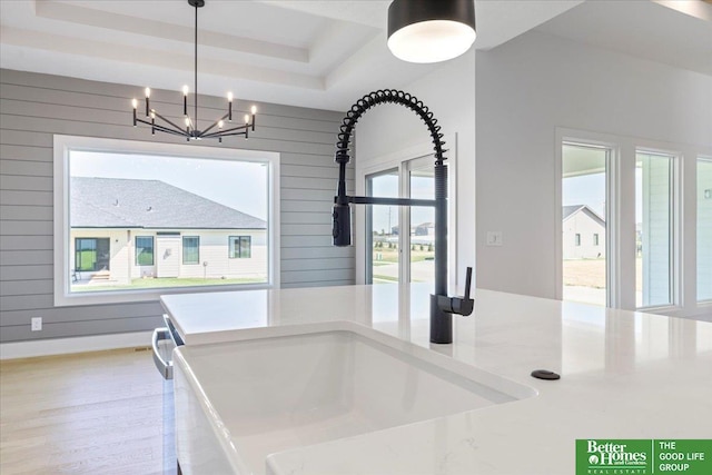 kitchen with sink, wooden walls, a tray ceiling, decorative light fixtures, and a chandelier