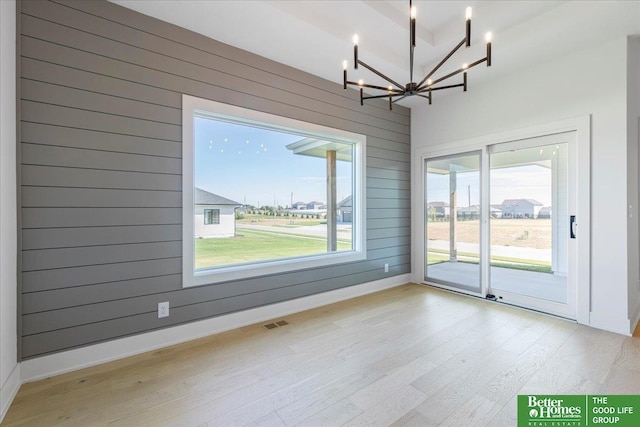 unfurnished dining area with wood walls, light hardwood / wood-style flooring, and an inviting chandelier