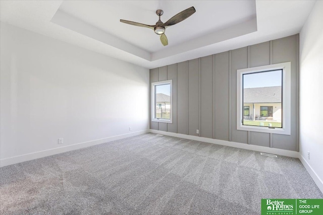 carpeted spare room with a tray ceiling and ceiling fan