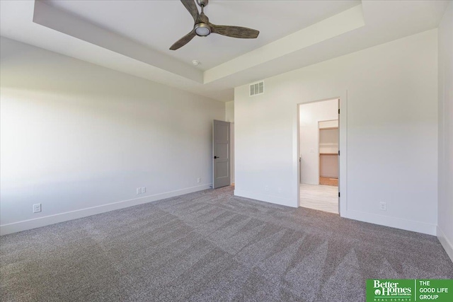 unfurnished bedroom featuring a tray ceiling, light colored carpet, ceiling fan, a spacious closet, and a closet