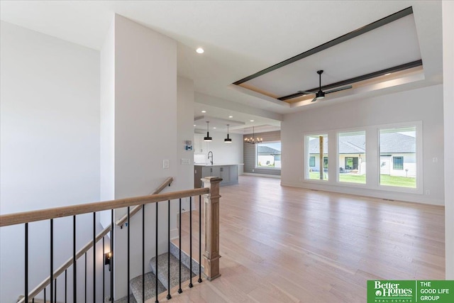 interior space featuring ceiling fan with notable chandelier, light wood-type flooring, sink, and a tray ceiling