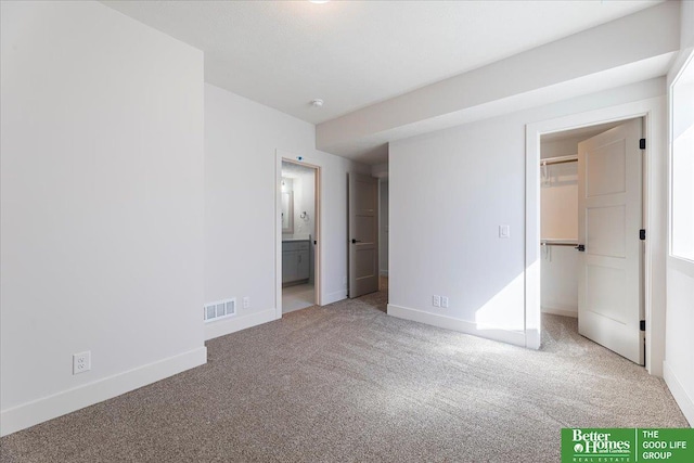 unfurnished bedroom featuring light colored carpet, a spacious closet, and ensuite bath