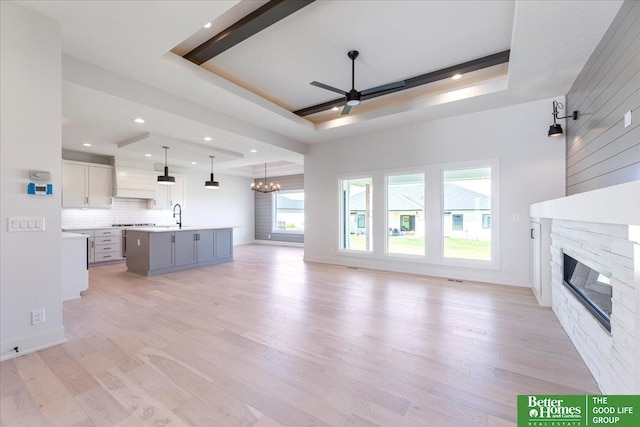 unfurnished living room featuring sink, ceiling fan with notable chandelier, a raised ceiling, and a fireplace