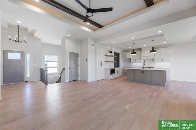 kitchen featuring decorative backsplash, a kitchen island with sink, white cabinets, light hardwood / wood-style floors, and hanging light fixtures