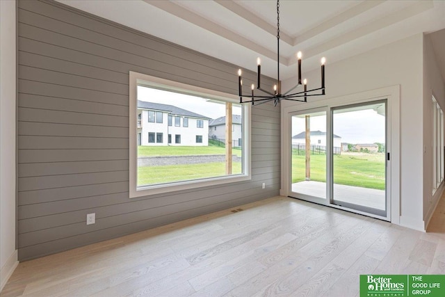 unfurnished dining area featuring a raised ceiling, wooden walls, a chandelier, and light wood-type flooring